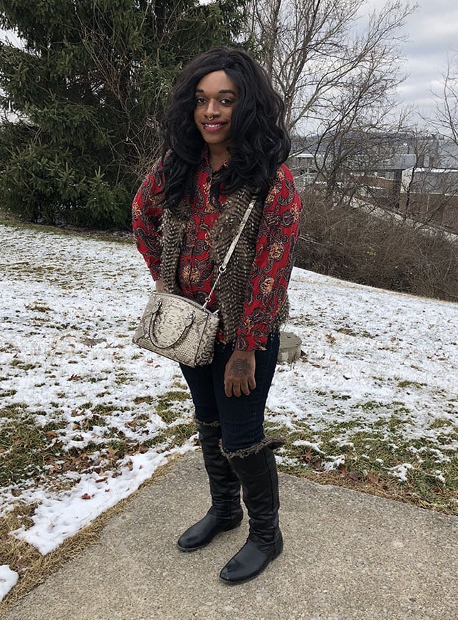 West Virginia University student Teddy sports a red patterned button-up blouse with a brown faux fur vest. He pairs his bold top with dark denim jeans and flat black fur-lined boots.